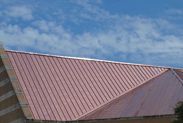 Close-up of aged standing seam copper roofing panels with a dark brown oxidized patina finish.
