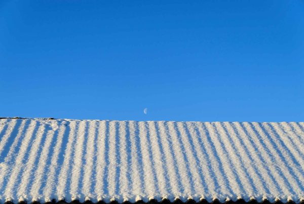 One sided corrugated metal roof covered with snow under an overcast sky.